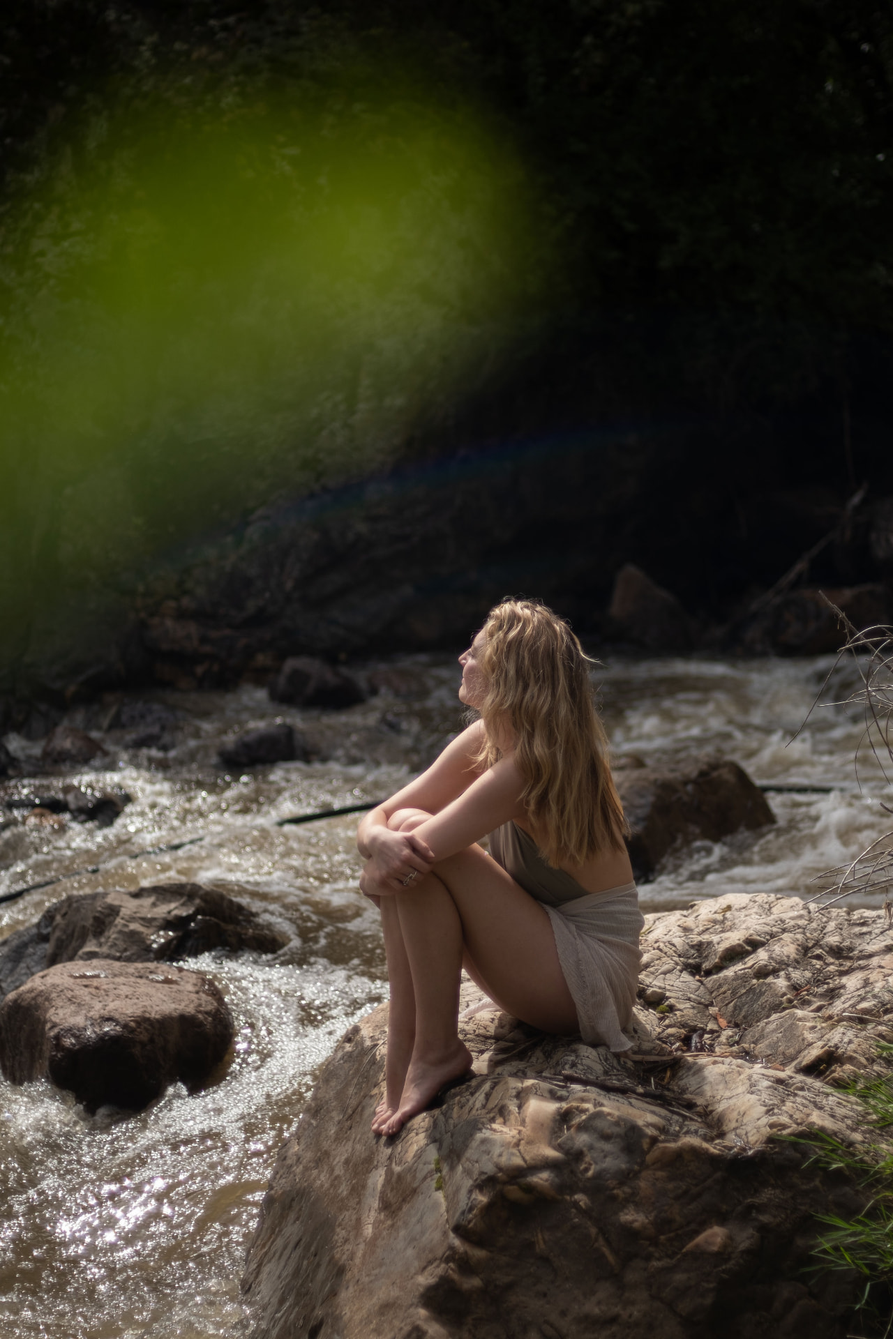 Ann-Sophie sitzt nachdenklich an einem sonnigen Waldbach